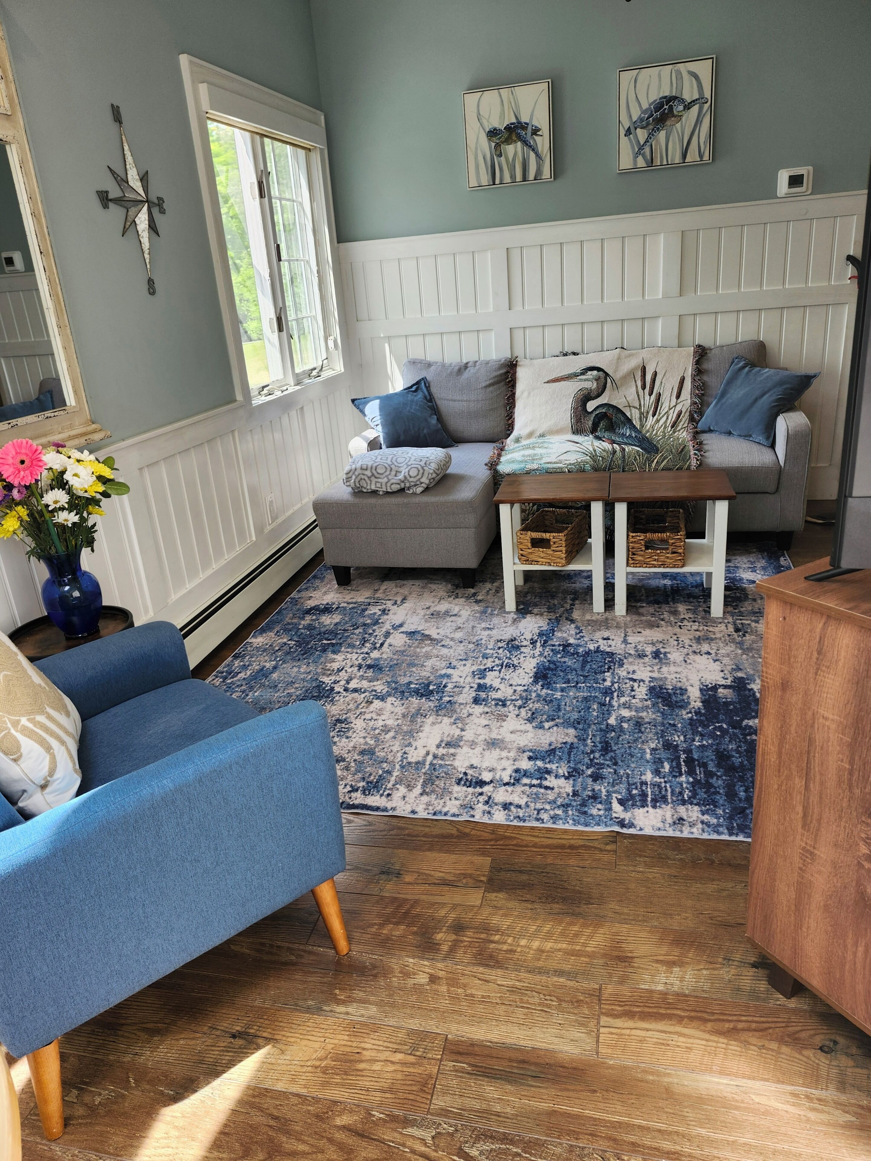 A living room with a blue armchair, a grey sofa, a coffee table, and a patterned rug.