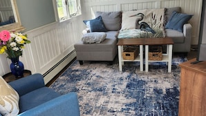 A living room with a blue armchair, a grey sofa, a coffee table, and a patterned rug.