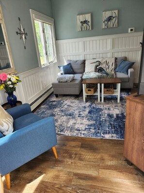 A living room with a blue armchair, a grey sofa, a coffee table, and a patterned rug.