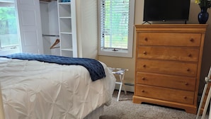 A bedroom with a bed, a dresser, a TV, a closet, and a window with blinds.