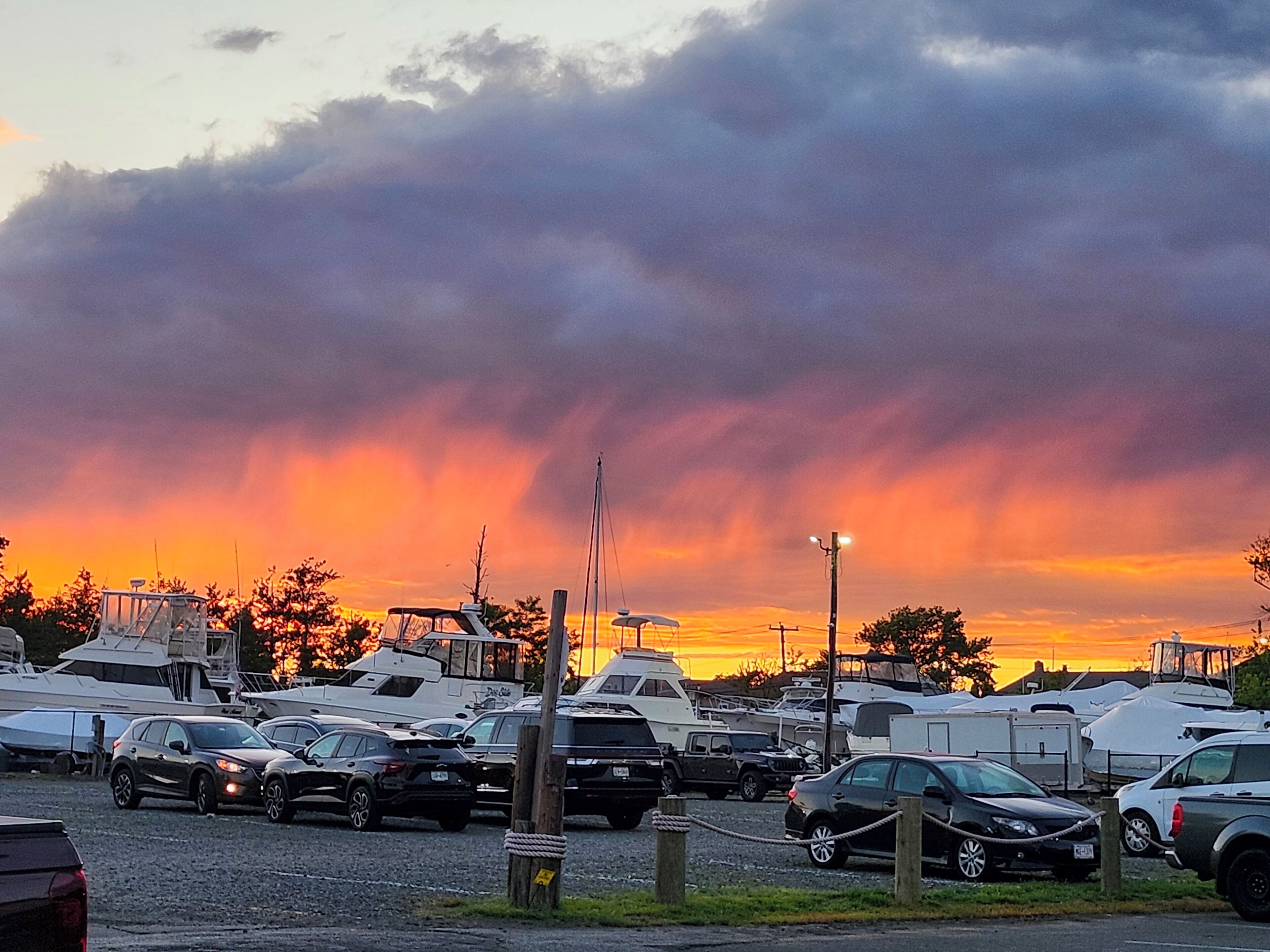 A marina with boats and cars parked, under a cloudy sky.