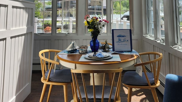 A dining area with a table, chairs, a vase with flowers, and a sign that reads 'Relax Unwind & Enjoy'.