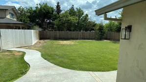 A backyard with a curved concrete pathway, a wooden fence, and a house in the background. - 3-possible 4 bedroom house in Modesto with plenty parking & space. (Modesto)