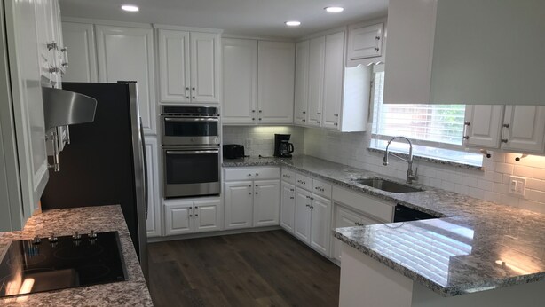 A modern kitchen with white cabinetry, stainless steel appliances, granite countertops, and a wooden floor. - 3-possible 4 bedroom house in Modesto with plenty parking & space. (Modesto)