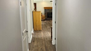 A hallway with wooden flooring, white walls, and doors leading to a living area with a fireplace. - 3-possible 4 bedroom house in Modesto with plenty parking & space. (Modesto)