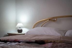 Ein Bett mit Kopfteil, ein Nachttisch mit Lampe und eine Wand.