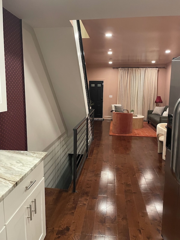 Een moderne woonkamer met een houten vloer, een trap, een eethoek met een tafel en stoelen, en een keuken met witte kastjes.