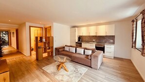 Ein modernes Wohnzimmer mit einer Couch, einem Glastisch und einer Küchenzeile mit Schränken und Geräten.