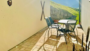 Eine Terrasse mit Tisch und Stühlen, einer Wanddekoration mit einem Hirschkopf und Blick auf ein Gebirge.