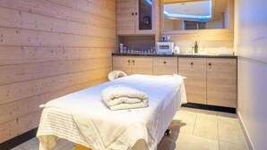A room with a wooden wall, a bed with a white blanket, a small bathroom with a mirror, and a ceiling light. - Alps Flat With Heated Pool (Araches-la-Frasse)