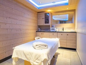 A room with a wooden wall, a bed with a white blanket, a small bathroom with a mirror, and a ceiling light. - Alps Flat With Heated Pool (Araches-la-Frasse)