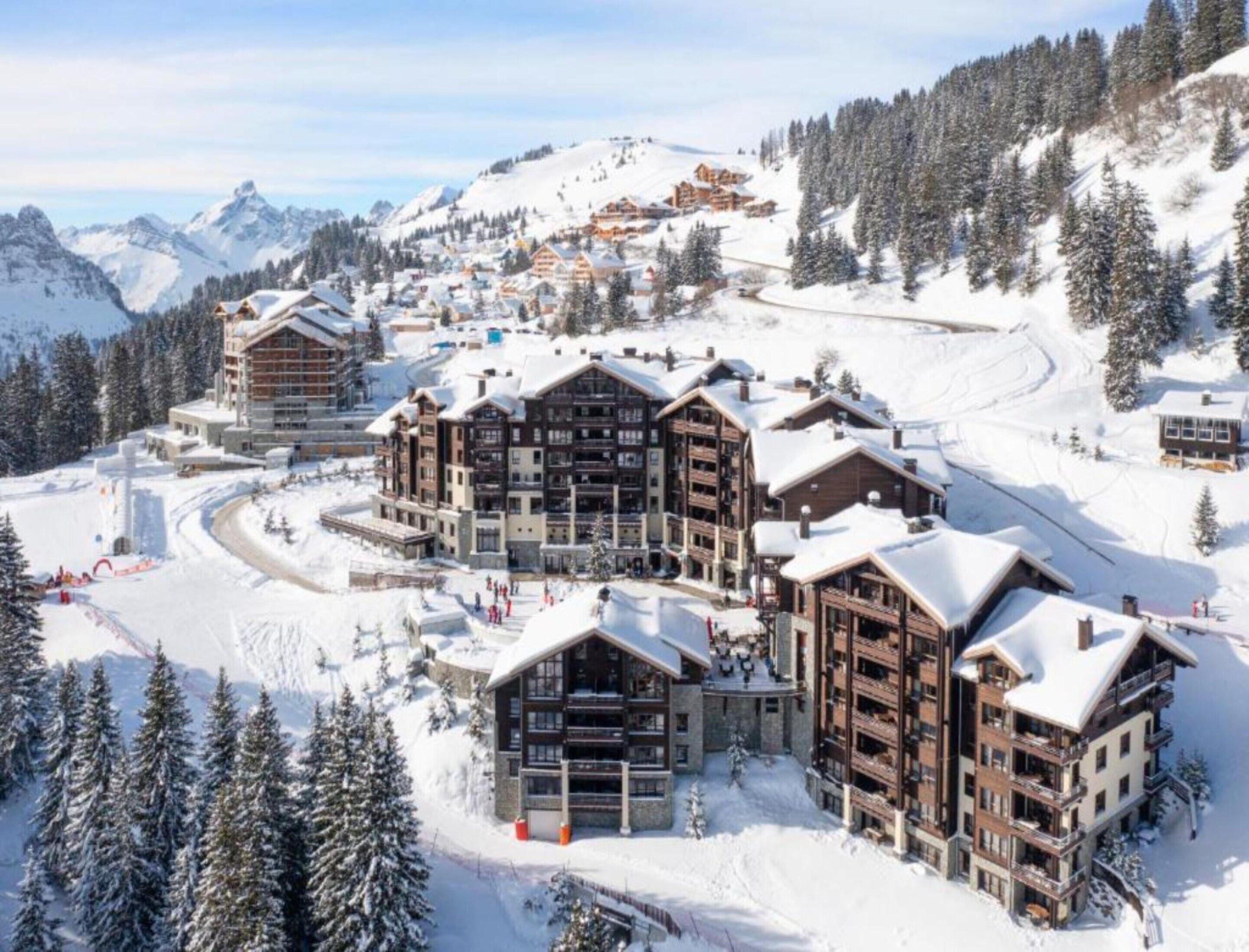 A ski resort with multiple multi-story buildings, ski slopes, and snow-covered trees.