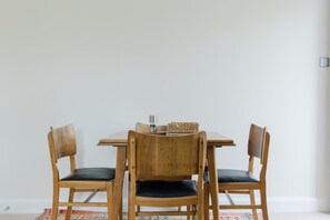 A dining table with four wooden chairs, a woven basket, and a small metal container on the table. - Tasteful 2BDR Midcentury Modern Home (London)