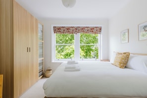 Une chambre à coucher avec un lit, une fenêtre donnant sur des arbres, une armoire et une table de chevet.