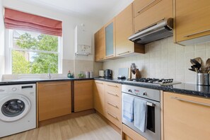 Eine moderne Küche mit Holzausbau, einer integrierten Waschmaschine, einem Herd und einem Fenster mit Blick auf Grünflächen.