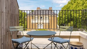 A balcony with a table and two chairs, a wooden fence, and a brick building in the background. - Tasteful 2BDR Midcentury Modern Home (London)