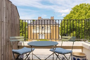 A balcony with a table and two chairs, a wooden fence, and a brick building in the background. - Tasteful 2BDR Midcentury Modern Home (London)