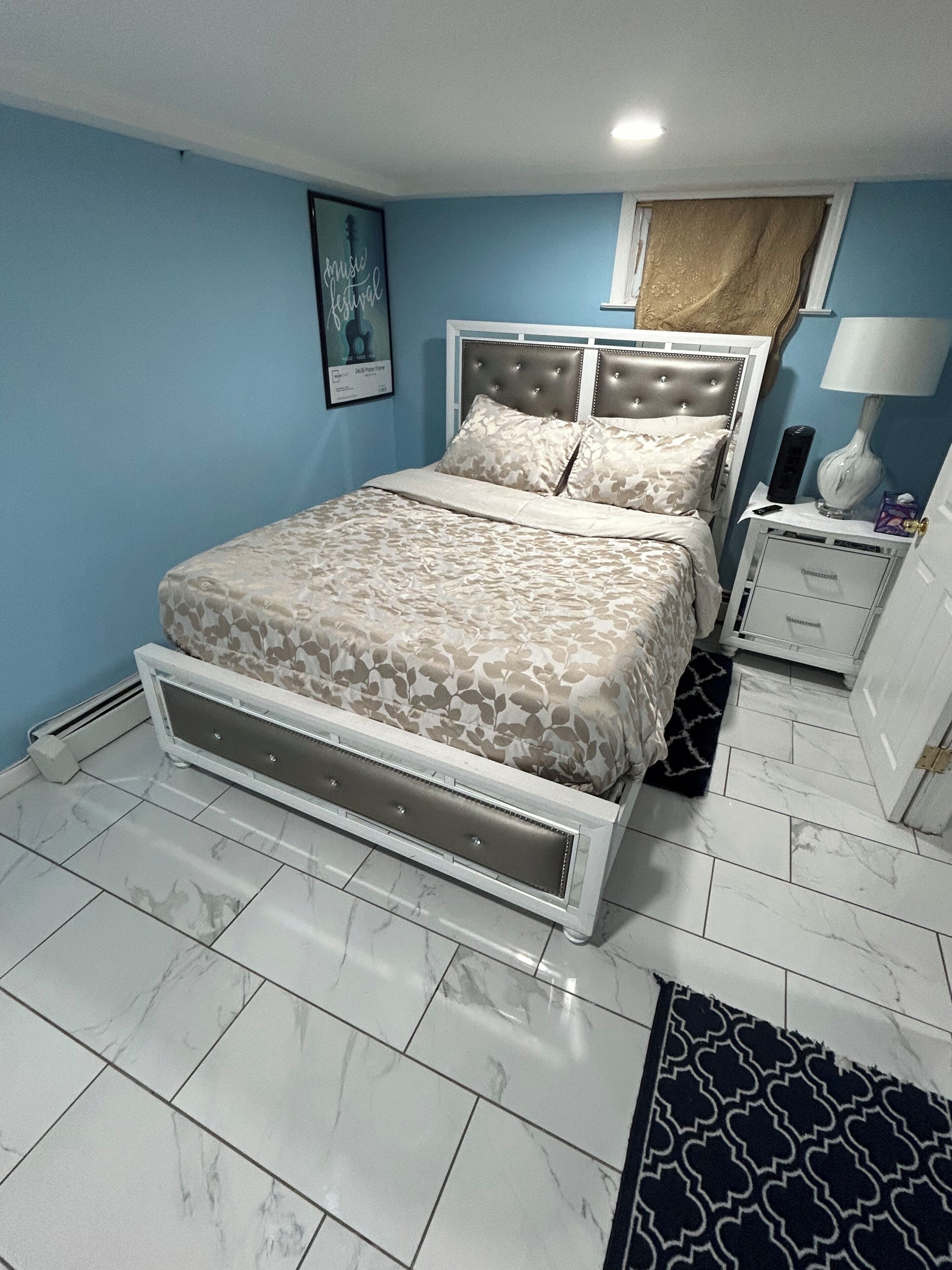 A bedroom with a bed, bedside tables, a lamp, a framed picture, and a patterned rug.
