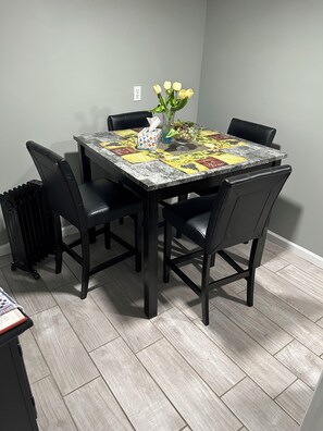 A dining table with a floral centerpiece, black chairs, and a patterned tablecloth. - Cozy 1-bedroom basement apartment suite in lovely Elmont with private entrance. (Elmont)