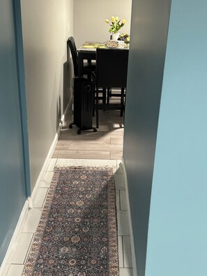 A hallway with a patterned rug, a table with a vase of flowers, and a suitcase. - Cozy 1-bedroom basement apartment suite in lovely Elmont with private entrance. (Elmont)