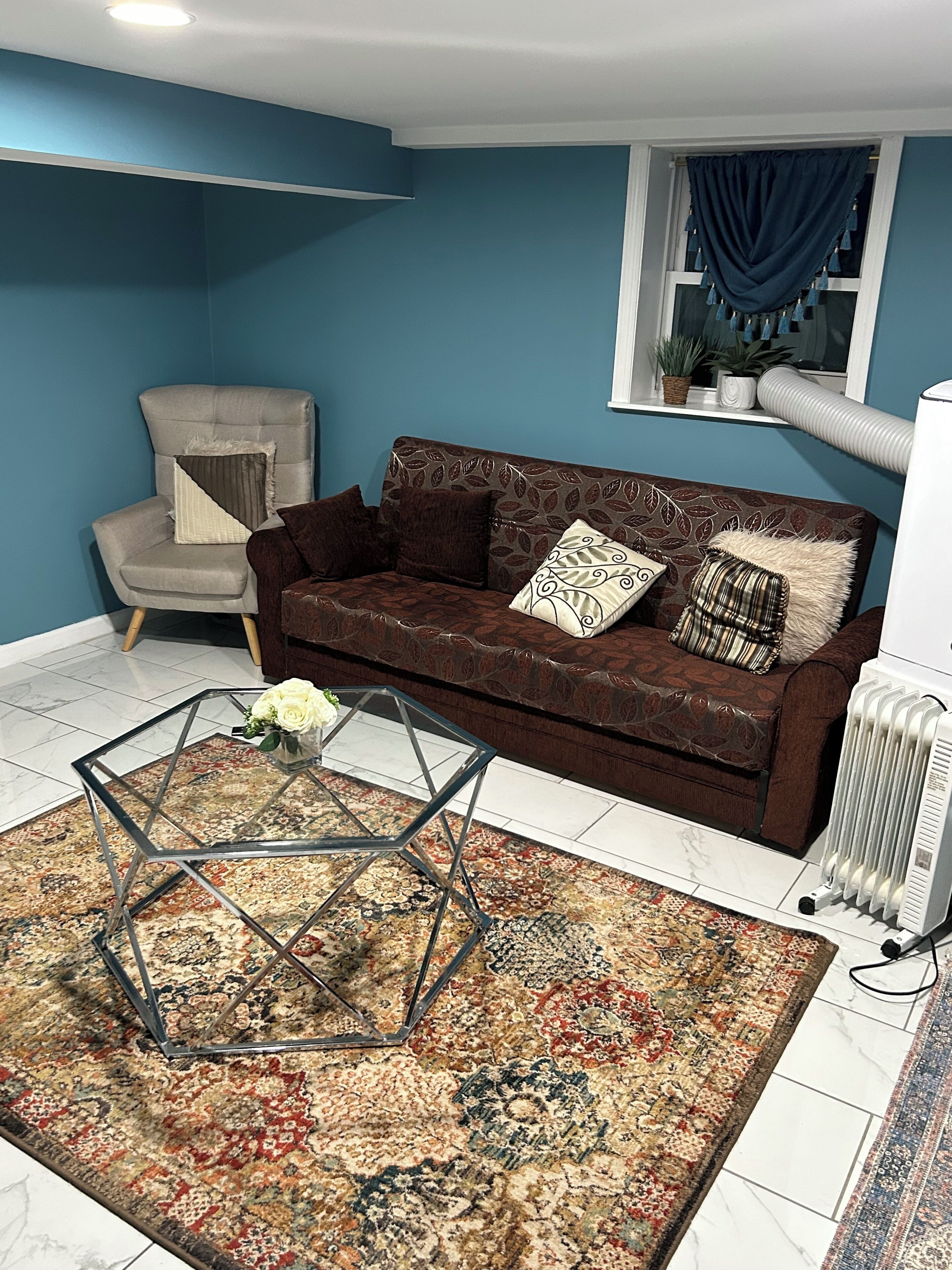 A living room with a brown sofa, a glass coffee table, a patterned rug, a blue wall, and a radiator.