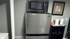 Una cocina con un refrigerador de acero inoxidable, un microondas, un basurero y una mesita con un marco de fotos.