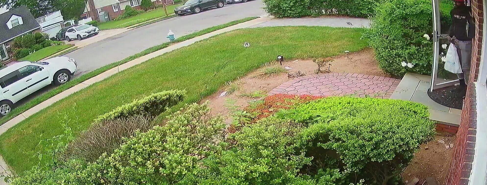 A residential street with houses, a driveway, and a lawn with a circular flower bed.