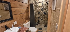 Un baño de madera con pared de ducha de piedra, un lavamanos y un inodoro.