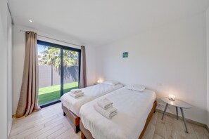 Ett sovrum med två sängar, ett litet bord med en lampa och en skjutdörr i glas som leder ut till en balkong.