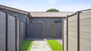 A gated backyard with a wooden deck, a small lawn, and a building with a tiled roof. - Lecci Retreat Near Cala Rossa Beach (Lecci)