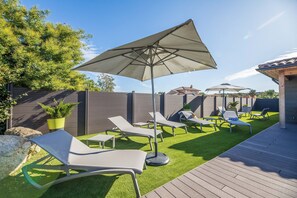 An outdoor patio with lounge chairs, a large umbrella, artificial grass, and a wooden deck. - Lecci Retreat Near Cala Rossa Beach (Lecci)