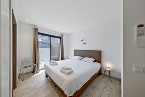Una habitación de hotel moderna con una cama grande, una silla, una mesita y una ventana con cortinas.