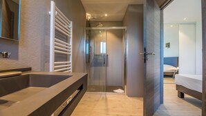 A modern bathroom with a large sink, a glass shower enclosure, and a visible bedroom with a bed and a door leading to another room. - Lecci Retreat Near Cala Rossa Beach (Lecci)