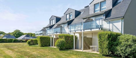 Uma fileira de casas modernas com varandas, sebes bem aparadas e um gramado bem cuidado.