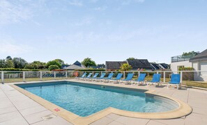 Una piscina con sillones reclinables azules y cielo despejado.