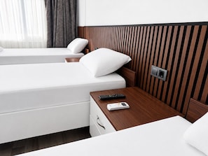 A hotel room with two beds, a wooden nightstand, a remote control, a thermostat, and a wall-mounted light switch.