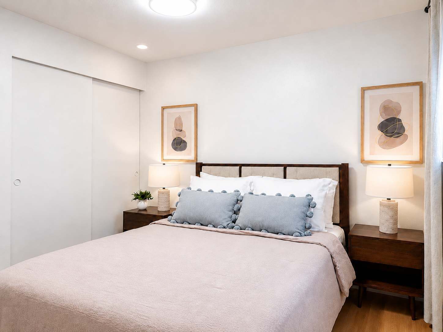 A bedroom with a bed, bedside tables, lamps, and framed artwork on the walls.
