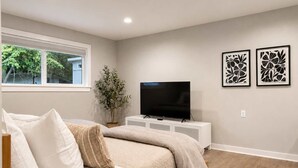 A bedroom with a bed, a TV, a potted plant, and two framed artworks on the wall. - Bellevue 2323, Whole house, Fenced Yard (Bellevue)