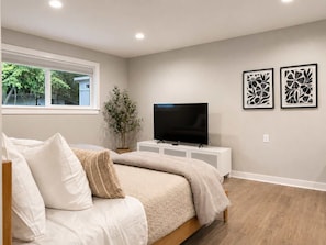A bedroom with a bed, a TV, a potted plant, and two framed artworks on the wall. - Bellevue 2323, Whole house, Fenced Yard (Bellevue)