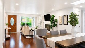 A modern living room with a fireplace, a dining area with a long table, and a TV mounted on the wall. - Bellevue 2323, Whole house, Fenced Yard (Bellevue)