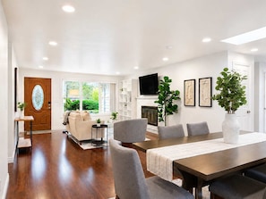 A modern living room with a fireplace, a dining area with a long table, and a TV mounted on the wall. - Bellevue 2323, Whole house, Fenced Yard (Bellevue)