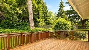 A wooden deck with a railing, surrounded by lush greenery and trees. - Bellevue 2323, Whole house, Fenced Yard (Bellevue)