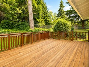 A wooden deck with a railing, surrounded by lush greenery and trees. - Bellevue 2323, Whole house, Fenced Yard (Bellevue)