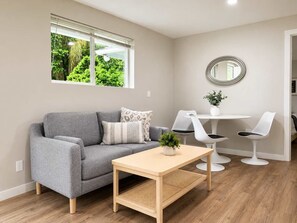 Ein modernes Wohnzimmer mit einem grauen Sofa, einem Holztisch und einem Essbereich in Weiß mit drei Stühlen.