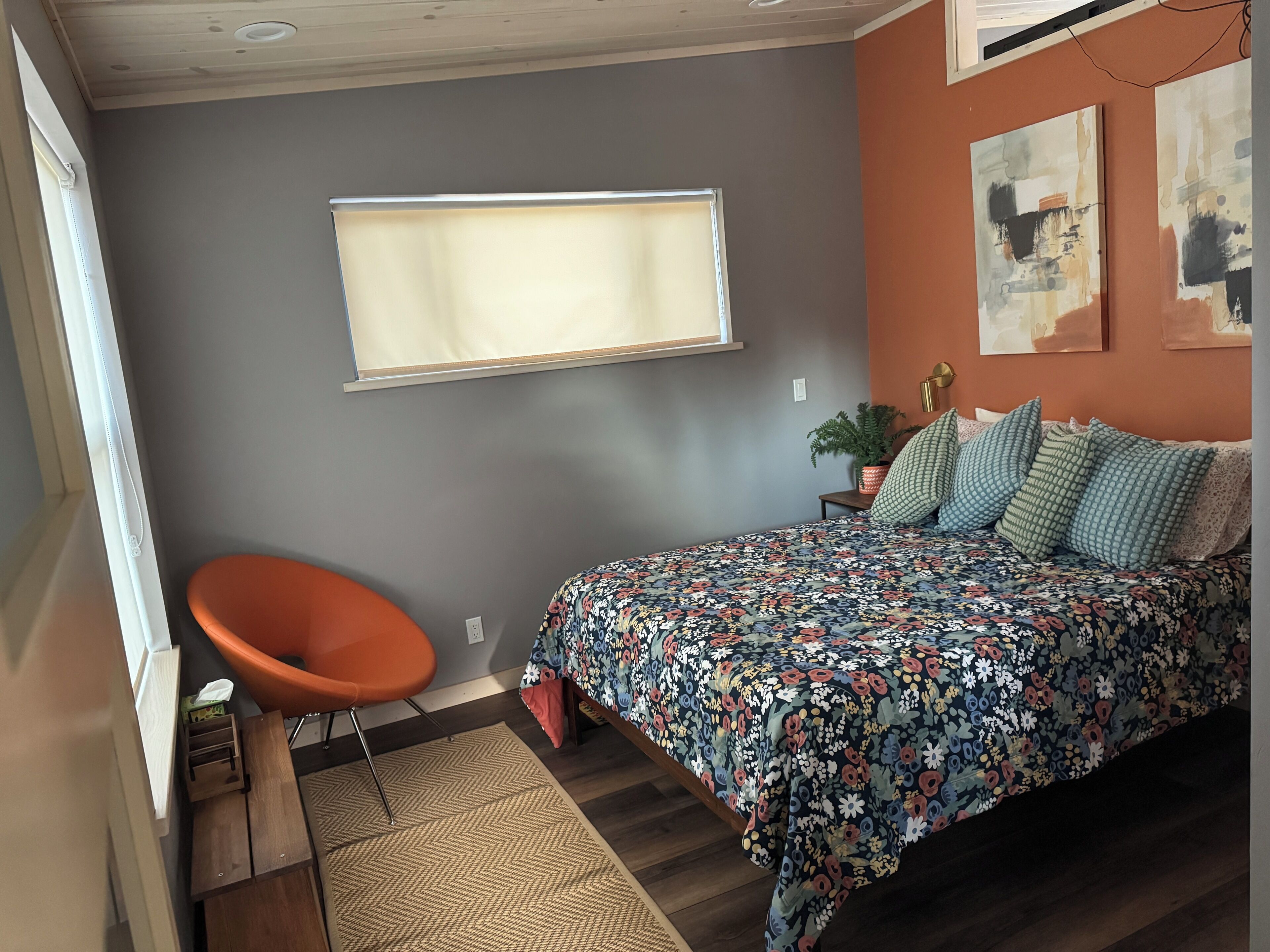 Un dormitorio con cama, una silla, un ventanal y una planta.