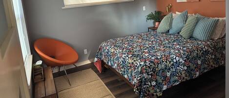 Un dormitorio con cama, una silla, un ventanal y una planta.