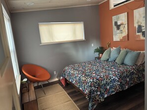 A bedroom with a bed, a chair, a window, and artwork on the wall.