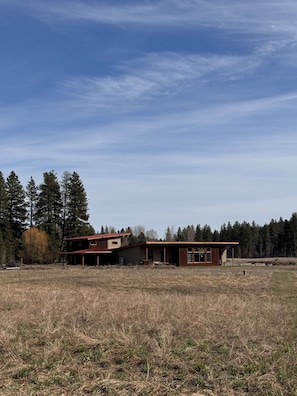 A two-story house with a garage, surrounded by a dry field and tall trees.