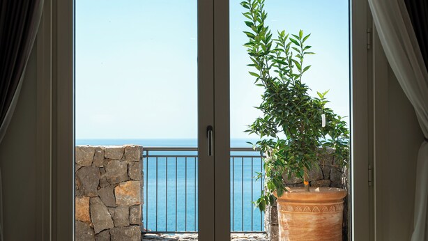 Ein Balkon mit Steinmauer, einer Kübelpflanze und Blick aufs Meer.