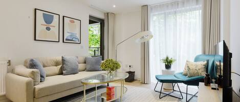A modern living room with a sofa, a glass coffee table, a blue accent chair, a TV, and artwork on the wall.